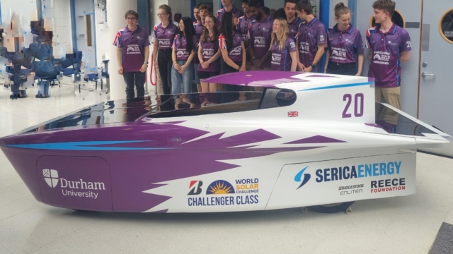 Purple and white solar car at Durham University. Group of students stood behind the solar car.